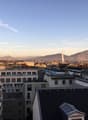Cityscape with multiple buildings, mountains in the background, and a fountain in the distance