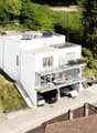 3-story modern white house with balconies, garage, and parking spaces, surrounded by trees and greenery