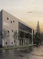 Office building, gray exterior, text 'BIEF 9', several windows, car parked in front, trees, sidewalk, people walking, another building in the background.