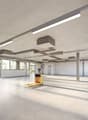Large open commercial space with concrete floors, exposed ceiling, and large windows. The space is equipped with overhead lighting fixtures and a yellow pallet jack in the center of the room.