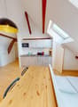 open floor plan, wooden table, two beds, one with a mattress, one with blankets, kitchen with sink and gas stove, microwave, refrigerator, and cabinets, large windows, attic beams, TV, hanging lamp