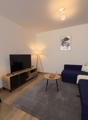 Living room with a blue sofa, wooden desk, TV, lamp, and rug
