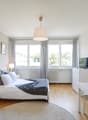 Bedroom with bed, pillows, blanket, lamps, TV, radiator, window, rug, chair, table, chairs