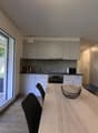 modern kitchen with dining area, large windows, wooden floor, white cabinets, modern appliances, dining table, chairs, couch with pillows
