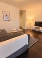 Living room with a gray sofa, two white pillows, a white coffee table, a floor lamp, a flat screen TV, a white entertainment center, a picture frame on the wall, and a rug.