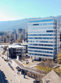 modern office building, mountains in the background, street with parked cars, greenery