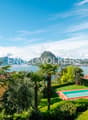 Luxury villa with swimming pool, surrounded by lush tropical gardens and palm trees, overlooking a scenic lake and mountains in the background.