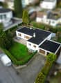 Detached house, single story, white walls, brown garage, paved driveway, garden, hedges, green grass, asphalt road