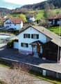 Detached house, white exterior, brown roof, attached garage, driveway, garden, multiple houses in the background