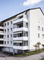 Multi-story apartment building with balconies and parking space.