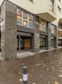 A multi-story commercial building with a modern, glass-fronted design. The building has a stone facade and a covered entrance. There are several businesses operating in the building, including Kita and Insign. The surrounding area has trees with autumn fo