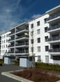 Multi-story apartment building with balconies, surrounded by landscaping and paved areas