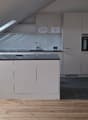 kitchen in attic with skylights, white cabinets, wooden floor, black countertop, oven, sink, faucet