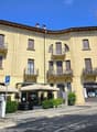 3-story building, yellow exterior, balconies on each floor, storefront with canopy, parking sign, greenery in front