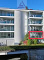Modern multi-story apartment building with glass balconies and terraces, surrounded by landscaping and a water feature.