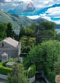 A two-story villa with a view of the mountains and lake, large landscaped garden, and a nearby road.