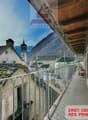 Balcony with stone walls, metal railing, roof with moss, street, view of a mountain and buildings.