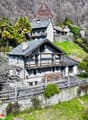 Stone house, multiple levels, wooden balcony, surrounded by trees, mountain view