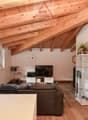 Living room with wooden ceiling, large window, sofa, TV, entertainment center, wooden floor, white walls, glass cabinet, potted plant
