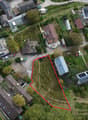 This image shows an aerial view of a residential area with a mix of houses, buildings, and gardens. There are several small plots of land or gardens visible, some of which appear to be used for growing crops or vegetables. There is also a parking area or
