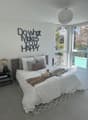 large bed with white duvet, grey and white pillows, black nightstand with books, lamp, round white lampshade, large windows overlooking pool