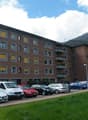 4-story building, red brick, many windows, several cars parked, grassy area, street light