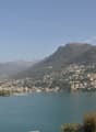 Scenic view of a mountainous town situated on the shores of a large lake, with blue waters and a clear sky in the background.