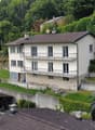 Detached house, multiple floors, tiled roof, exterior balconies, walled terrace, neighboring houses visible, situated on a slope with retaining walls