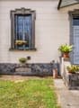 Traditional house, cream painted exterior, stone wall base, front door with window, step, several plants and flowers in front