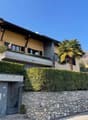 Detached house, beige painted exterior, small balcony, large garage, landscaped hedges, mature trees