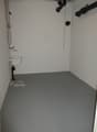 Empty basement, white walls, gray floor, white sink, small sink drain, plumbing pipes