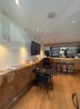 A room with a wooden floor, a counter, a table, chairs, a television, and a refrigerator.