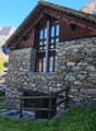 Old house made of stone, with a solar panel on the roof, wooden door, two windows, surrounded by lush green grass