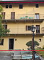 Three story house, yellow, two balconies with chairs, streetlight, entry door, bike rack