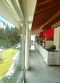 Spacious kitchen with large windows overlooking a garden, wooden ceiling beams, white cabinets and drawers, red accent wall, dining table and chairs