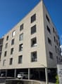 Contemporary apartment building, multiple floors, modern design, several windows, underground parking area, and signage indicating residence.
