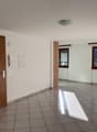 Empty room, white walls, tiled floor, two windows, wooden door, two switches, and telephone mounted on the wall.