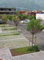 paved parking area with grass, concrete flowerbed, and two parked cars, building at a distance with mountain