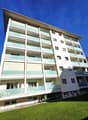 Apartment building, 6 floors, balconies on each floor, garden in front, mountains in the background