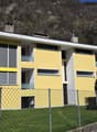 3 story yellow house, white trim, multiple windows, fenced yard, mountain in background