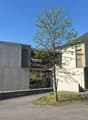 Modern concrete building, two-story, with a driveway, and a tree in the center