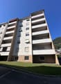 multi-story building, white exterior, balconies, windows with shutters, green lawn in front