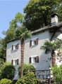 White building, brown shutters, steep slope roof, surrounded by trees, wooden fence, red pole, mountain in background