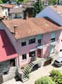 pink house with multiple balconies and red roof, two chimneys visible, large garden in front, street
