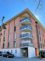 modern apartment building, brick exterior, balconies, street-level garage, several cars parked in front