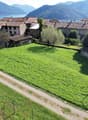 large grassy field, path, green shrubs, small brick structure, trees
