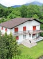 2 story house, white exterior, brown roof, balcony, large front yard, surrounded by trees, grassy area