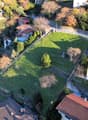 Aerial view of a residential area with several houses, a large grassy field, and a road.