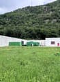 white building, green containers, red doors, large grassy field, mountain in the background