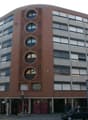 Multi-story brick building with large windows, circular window patterns, and ground-level retail spaces